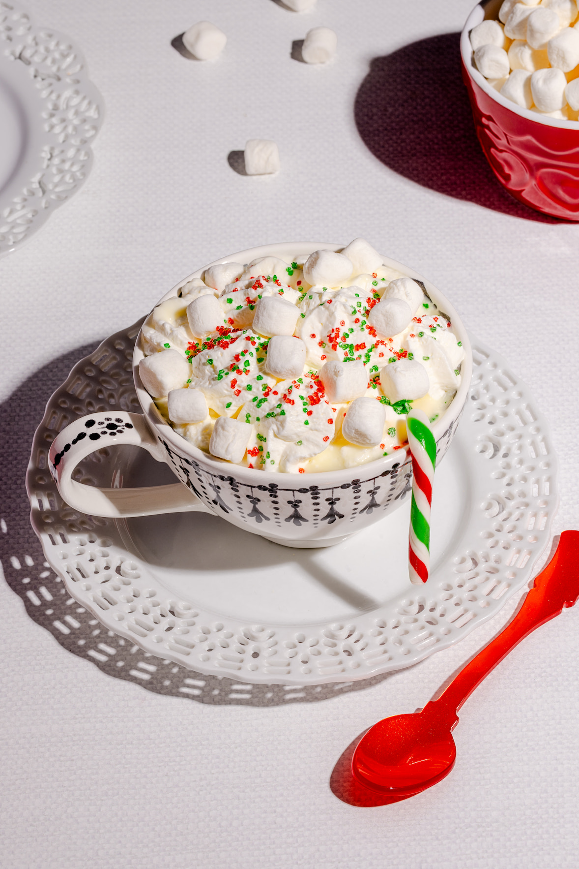 Chocolat chaud blanc gourmand garni de crème fouettée, mini guimauves et cannes de bonbons festives