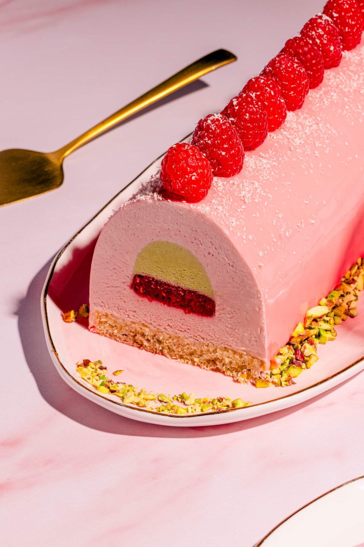 Bûche aux framboises et aux pistaches avec glaçage miroir au chocolat blanc