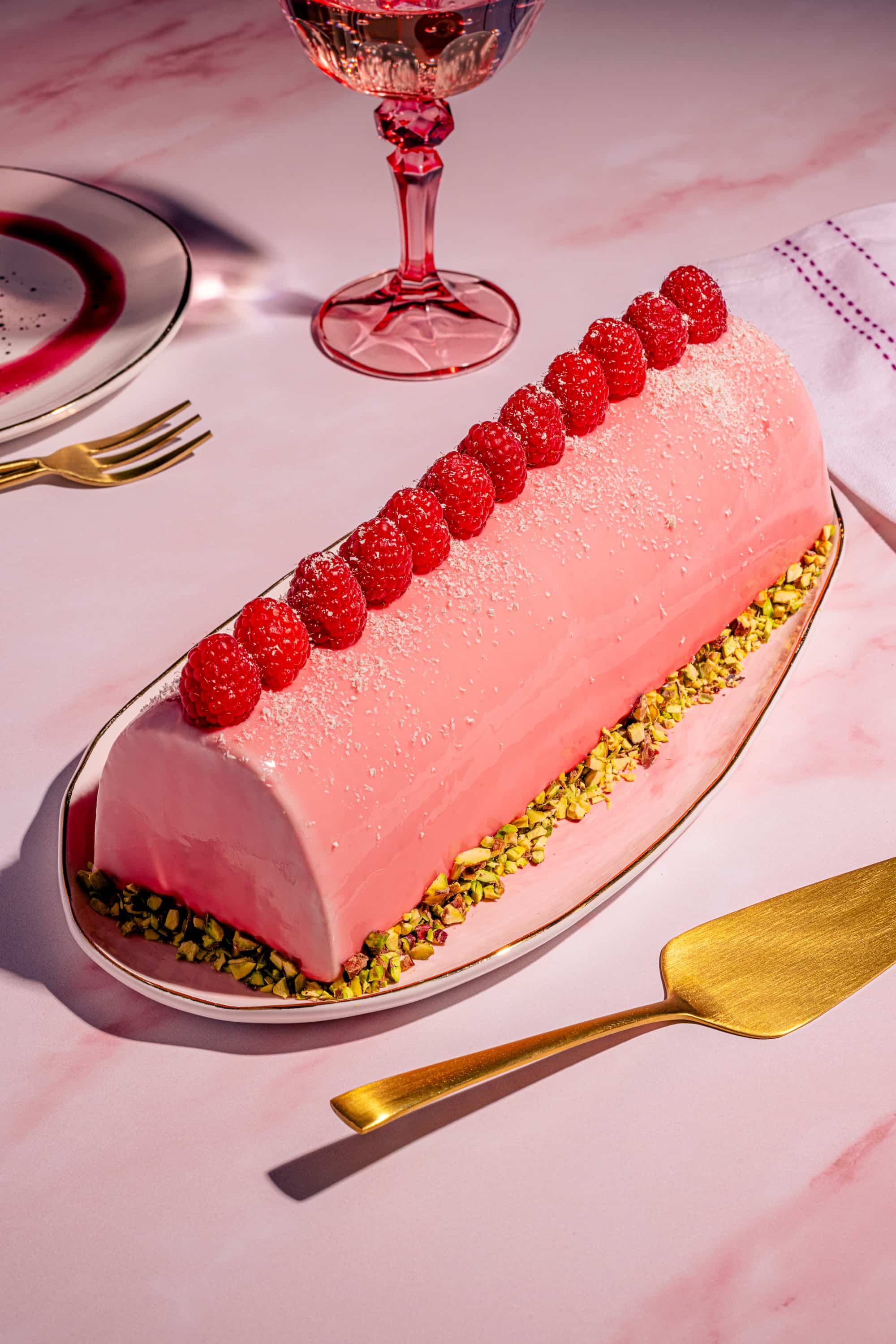 Bûche aux framboises et aux pistaches avec glaçage miroir au chocolat blanc