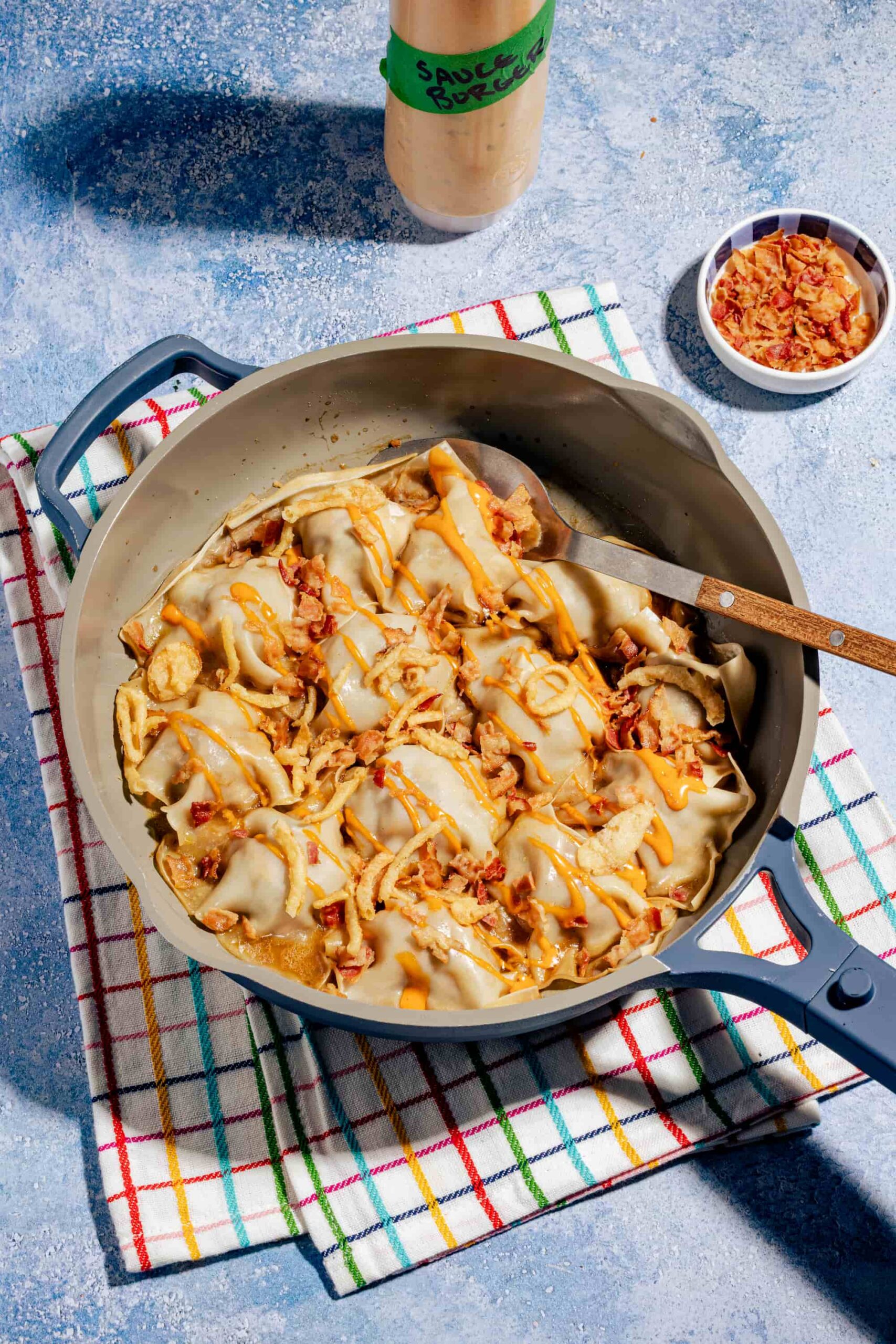 Dumplings rapides à la poêle façon cheeseburger, dorés et garnis de bœuf haché et de fromage fondant, servis dans une poêle bleue.